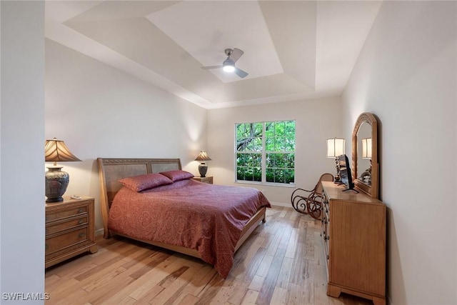 bedroom with light wood-type flooring, a raised ceiling, baseboards, and a ceiling fan