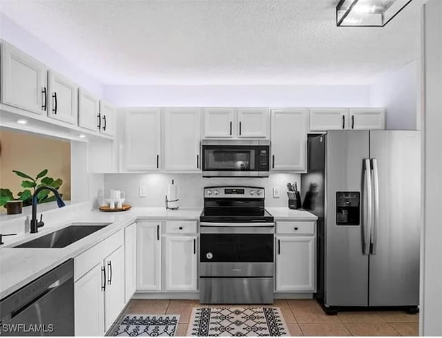 kitchen featuring light tile patterned floors, a sink, stainless steel appliances, light countertops, and white cabinets