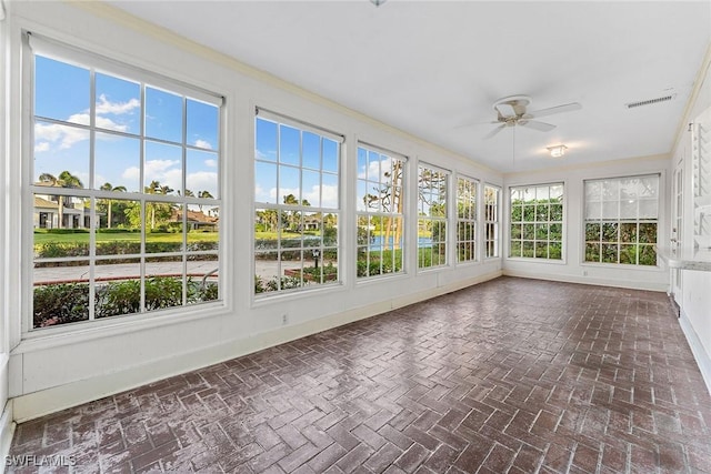 unfurnished sunroom featuring visible vents, a healthy amount of sunlight, and ceiling fan