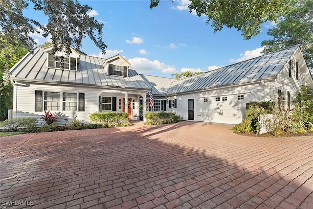 cape cod-style house with a garage, metal roof, decorative driveway, and a standing seam roof