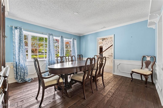 dining area featuring wainscoting, a textured ceiling, ornamental molding, and dark wood-style flooring