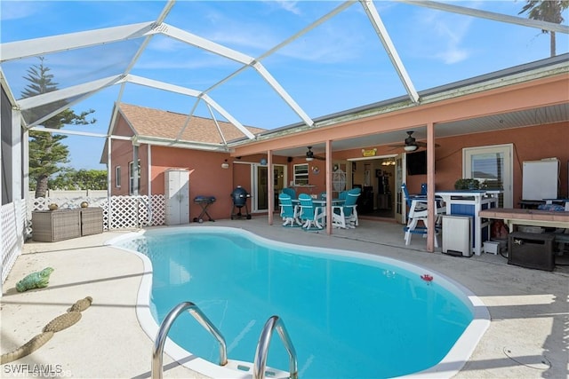 pool with glass enclosure, a patio, outdoor dining area, and a ceiling fan