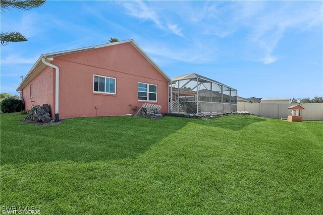 rear view of property with stucco siding, a yard, glass enclosure, and fence