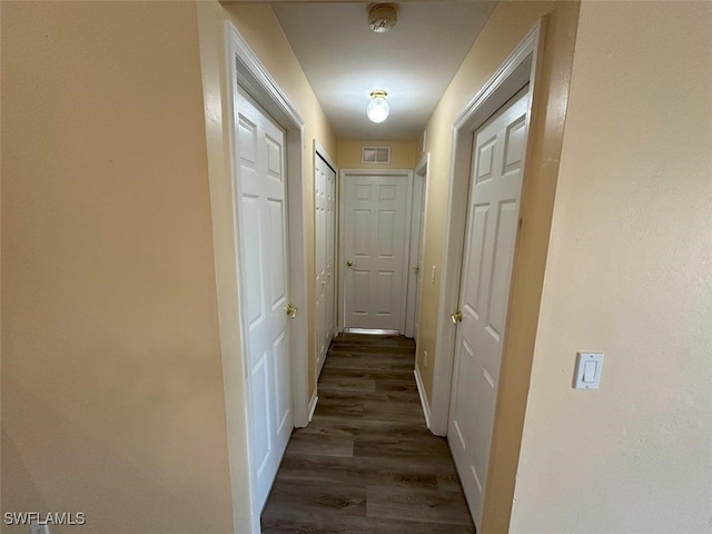 corridor featuring visible vents, baseboards, and dark wood-style flooring