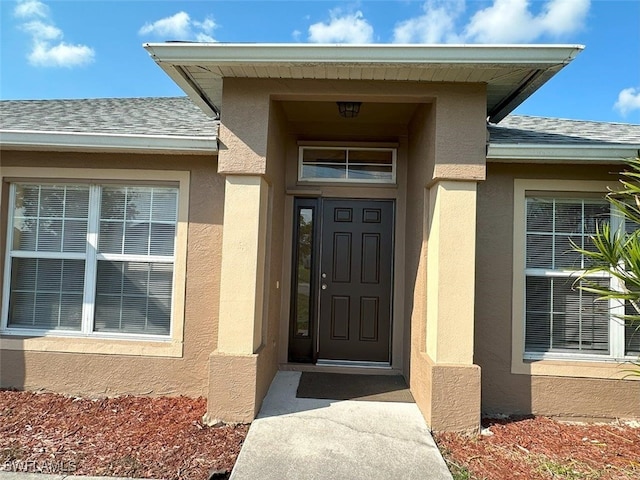 property entrance with stucco siding and a shingled roof