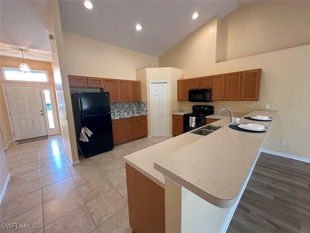 kitchen featuring baseboards, black appliances, a peninsula, and brown cabinetry