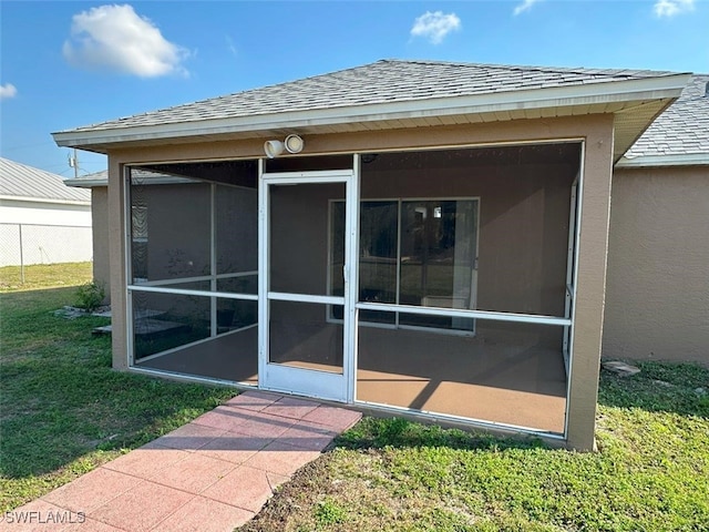 exterior space with a lawn, fence, roof with shingles, and stucco siding