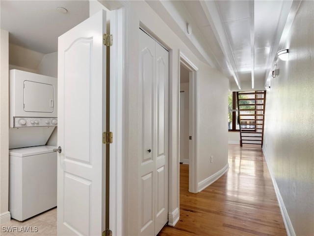 hall with baseboards, light wood-style floors, and stacked washer and dryer