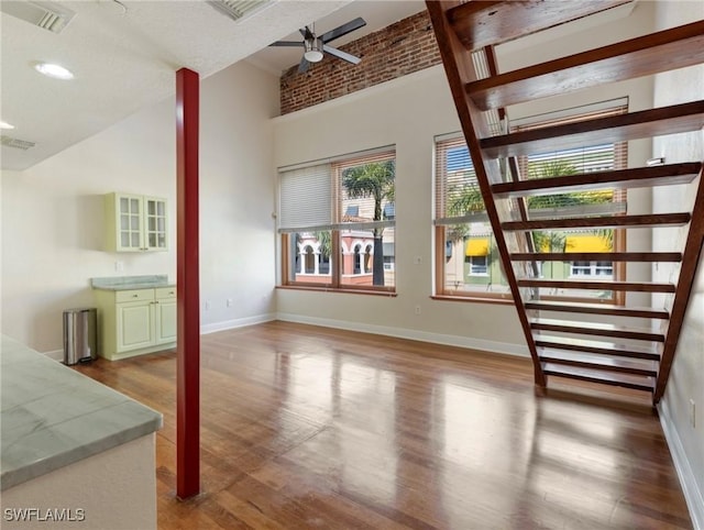 unfurnished living room with a ceiling fan, a high ceiling, wood finished floors, and visible vents