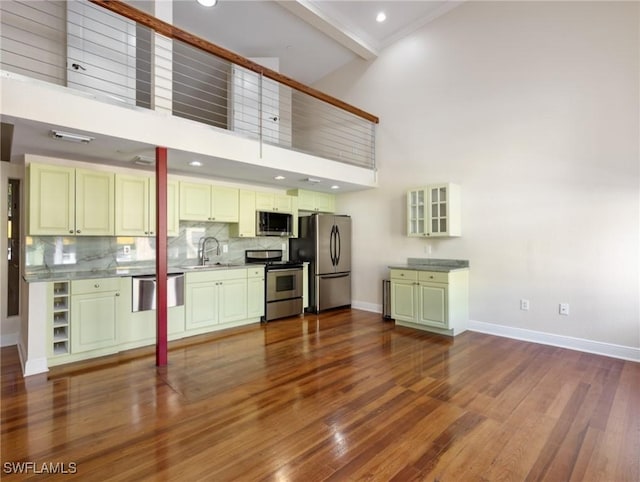 kitchen featuring a high ceiling, a sink, decorative backsplash, dark wood-type flooring, and stainless steel appliances