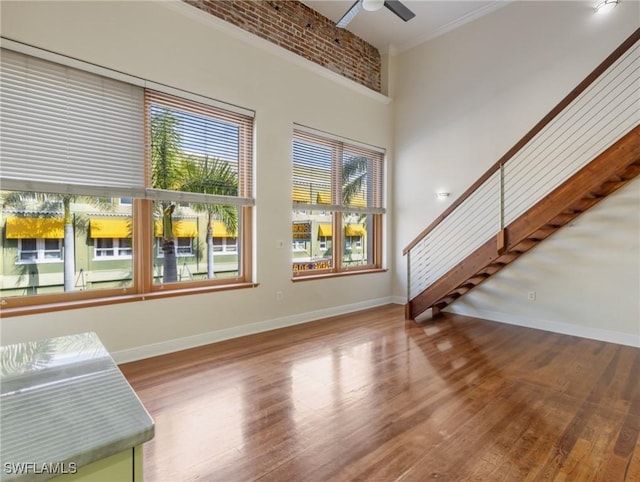 living room featuring ceiling fan, baseboards, stairway, a high ceiling, and wood finished floors