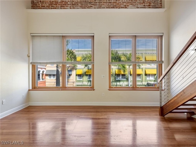 empty room with a healthy amount of sunlight, stairs, baseboards, and wood finished floors