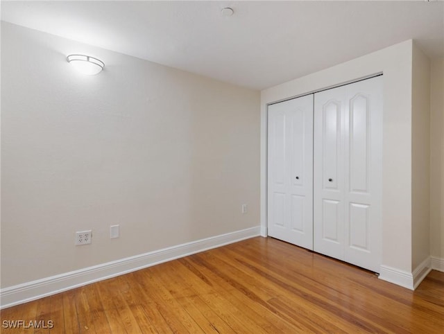 unfurnished bedroom featuring light wood finished floors, a closet, and baseboards