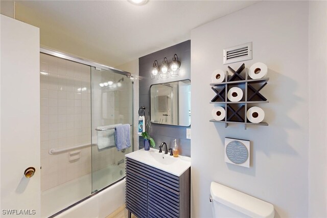 bathroom featuring visible vents, backsplash, bath / shower combo with glass door, toilet, and vanity