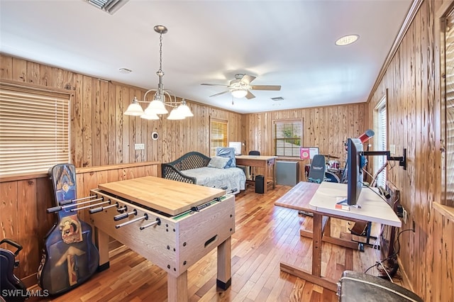 recreation room featuring visible vents, ceiling fan with notable chandelier, wood walls, and wood-type flooring