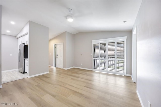 empty room featuring light wood finished floors, baseboards, and lofted ceiling