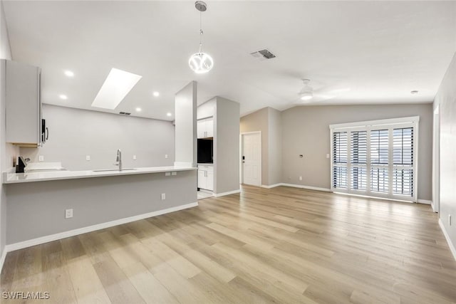 unfurnished living room with vaulted ceiling with skylight, light wood-style flooring, baseboards, and a sink