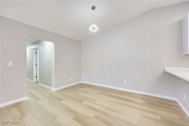 empty room with baseboards, lofted ceiling, and light wood-style floors