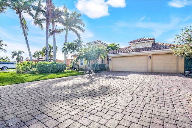 mediterranean / spanish home with a tiled roof, stucco siding, an attached garage, and decorative driveway