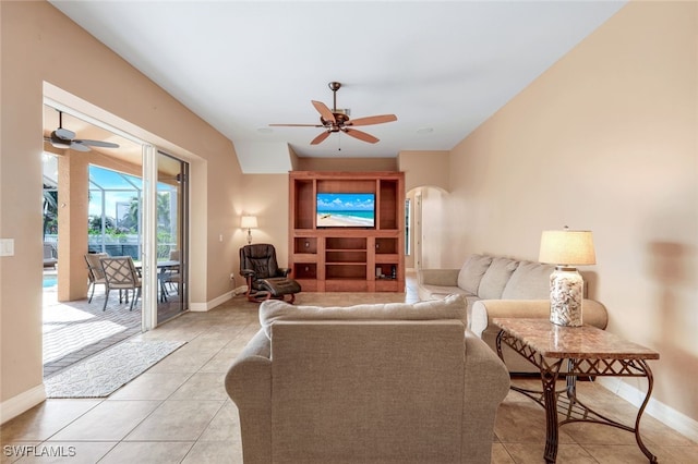 living room with baseboards, arched walkways, light tile patterned flooring, and a ceiling fan