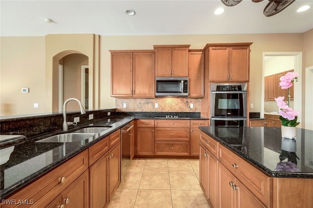 kitchen with brown cabinets, a sink, backsplash, appliances with stainless steel finishes, and light tile patterned floors