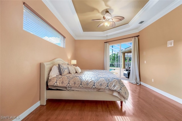 bedroom featuring a raised ceiling, ornamental molding, wood finished floors, baseboards, and access to exterior