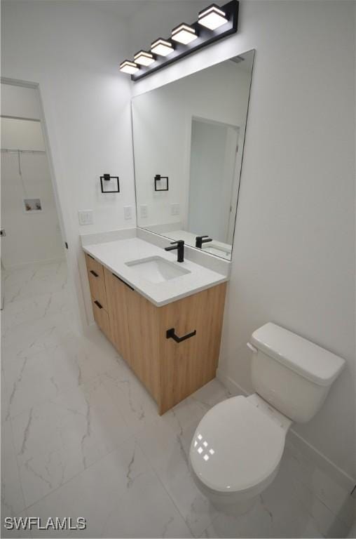 bathroom with vanity, toilet, baseboards, and marble finish floor