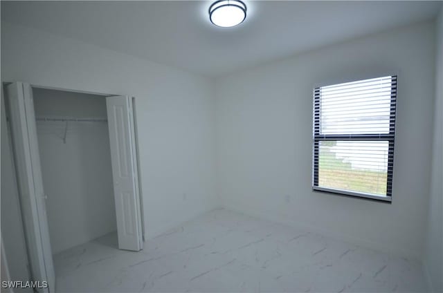 unfurnished bedroom with a closet, baseboards, and marble finish floor