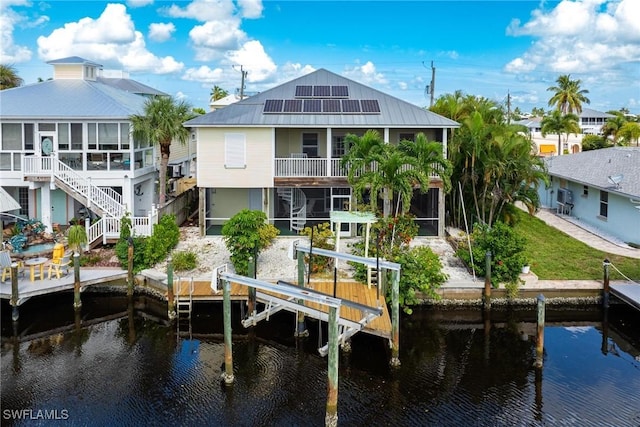 rear view of property featuring a water view, a sunroom, metal roof, boat lift, and solar panels