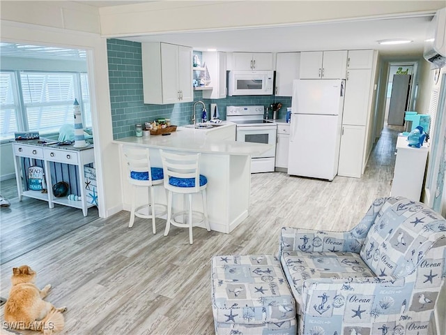 kitchen featuring white appliances, a peninsula, light wood finished floors, and a sink