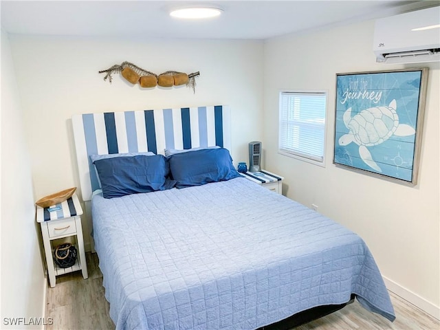 bedroom with a wall mounted air conditioner, baseboards, and wood finished floors