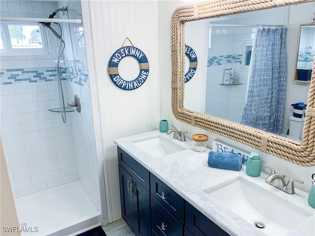 full bath with a tile shower, double vanity, and a sink