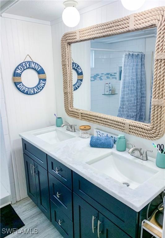 bathroom with a shower with shower curtain, double vanity, wood finished floors, and a sink