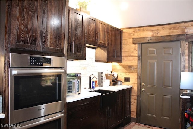 kitchen with dark brown cabinets, a toaster, wood walls, double oven, and light countertops