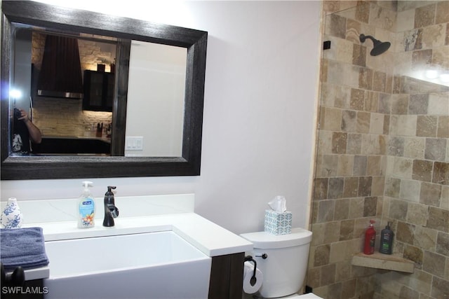 full bathroom with a tile shower, toilet, and vanity