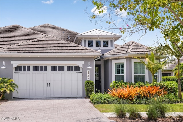 view of front of home with a tiled roof, decorative driveway, an attached garage, and stucco siding