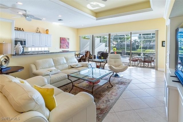 living area with light tile patterned floors, a tray ceiling, a ceiling fan, and a sunroom