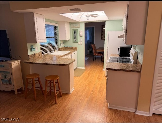 kitchen featuring a breakfast bar, light wood-style flooring, a peninsula, white cabinetry, and a sink