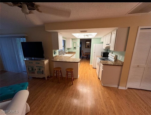 kitchen featuring light wood-type flooring, a breakfast bar, a textured ceiling, white appliances, and a peninsula