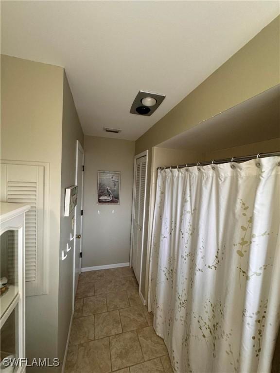 corridor with light tile patterned flooring, visible vents, and baseboards