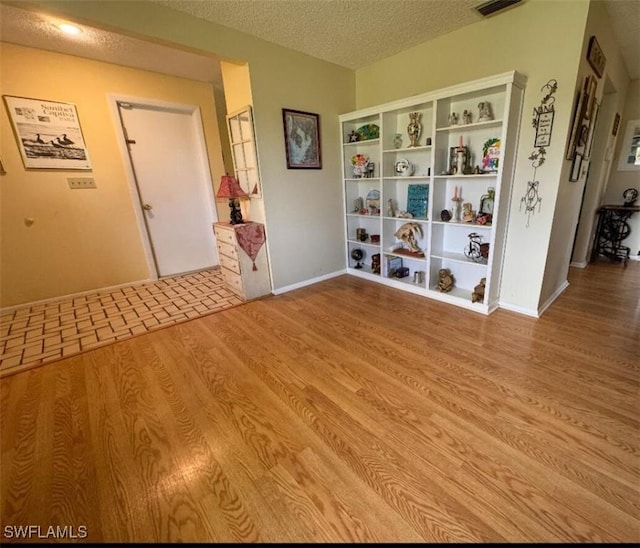 interior space with baseboards, wood finished floors, visible vents, and a textured ceiling