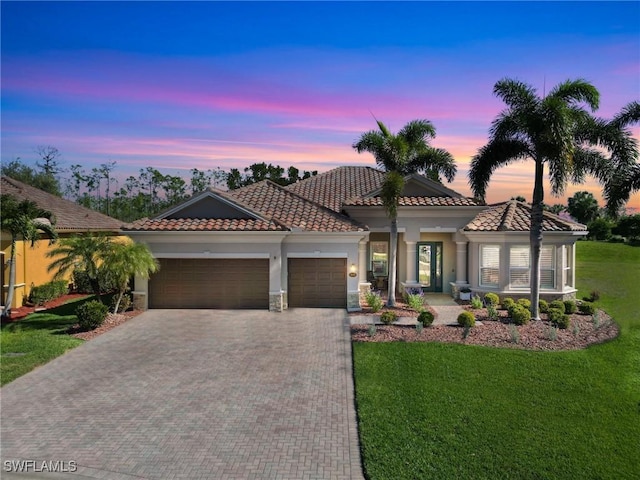 mediterranean / spanish-style house featuring a front lawn, a tiled roof, decorative driveway, and a garage