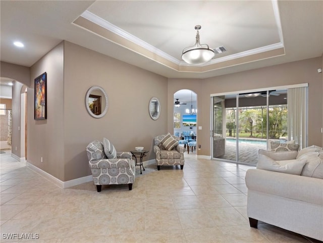 living room with a tray ceiling, visible vents, arched walkways, and ceiling fan