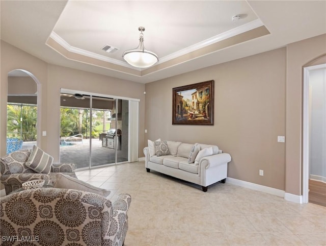 living area with a tray ceiling, baseboards, visible vents, and arched walkways