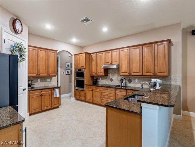 kitchen with visible vents, a sink, under cabinet range hood, double oven, and a peninsula