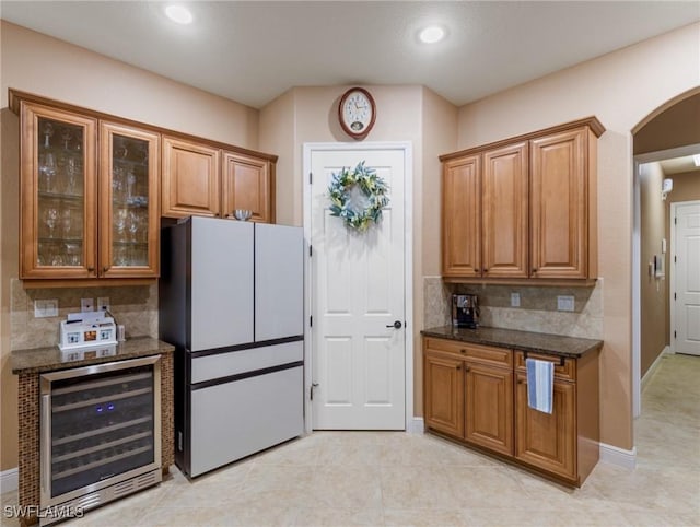 kitchen featuring wine cooler, brown cabinetry, arched walkways, and freestanding refrigerator