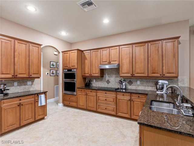 kitchen featuring visible vents, under cabinet range hood, a sink, double oven, and brown cabinetry