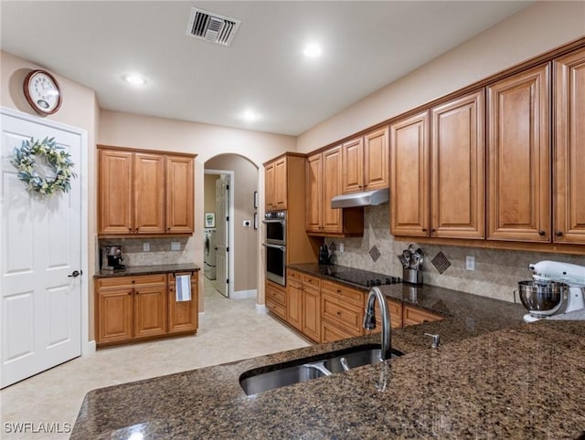 kitchen with visible vents, under cabinet range hood, arched walkways, black electric cooktop, and a sink