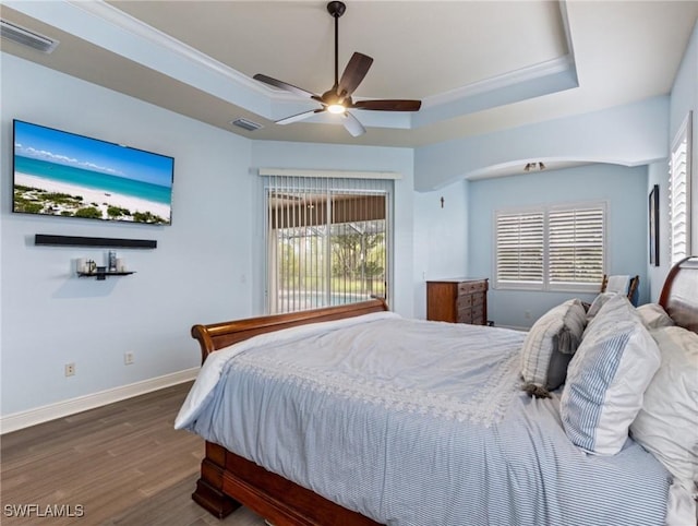 bedroom with visible vents, crown molding, baseboards, a tray ceiling, and wood finished floors