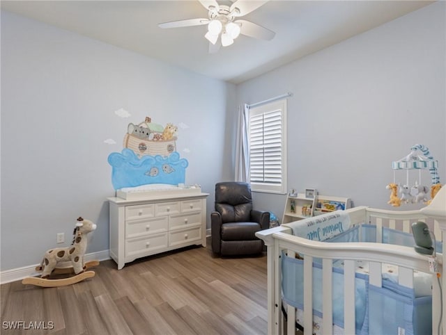 bedroom featuring a crib, light wood-style flooring, baseboards, and ceiling fan